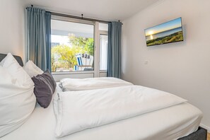 A hotel room with a bed, a window with curtains, and a painting of a beach scene.