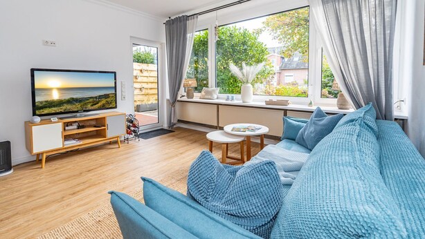A modern living room with a large TV, a sofa set, and a window with curtains. - This one love - Cozy vacation apartment for up to 3 people in Alt (Sylt)