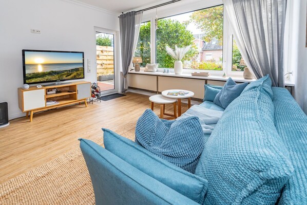 A modern living room with a large TV, a sofa set, and a window with curtains.