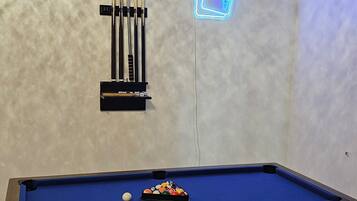 A pool table with a blue felt surface, a set of pool cues, and a neon sign on the wall.
