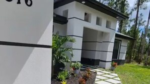 A modern building with a number '816' on the side, a paved pathway leading to the entrance, and a small garden with plants and flowers.