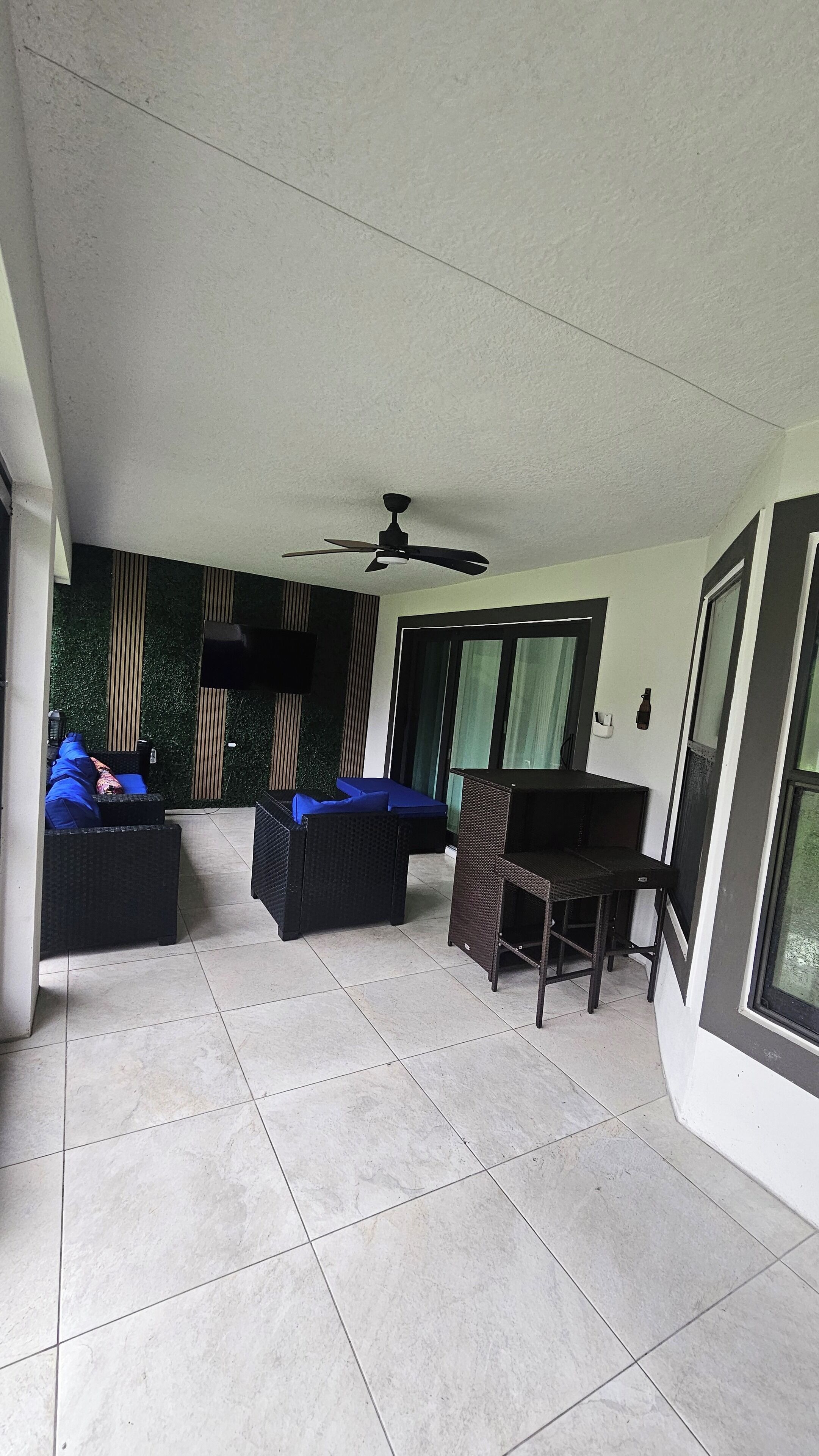 A spacious indoor area with tiled flooring, black wicker furniture, a ceiling fan, and a green wall with vertical stripes.
