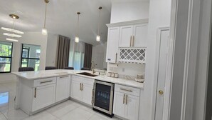 A modern kitchen with white cabinetry, a marble countertop, and pendant lighting.