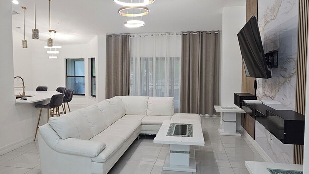 A modern living room with a white sectional sofa, a coffee table, and a TV mounted on the wall.