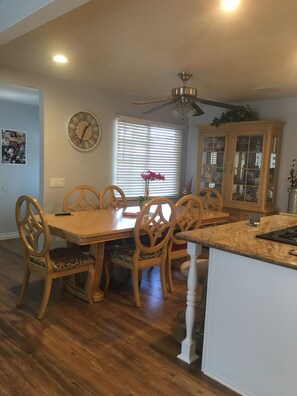 A dining area with a wooden table and chairs, a ceiling fan, a clock, and a window with blinds. - 3-bedroom house in East Whittier with AC/heating for a relaxing stay any season! (Whittier)