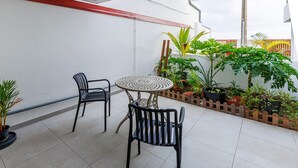 En terrasse med to stole og et bord, omgivet af krukker med planter og et træhegn.
