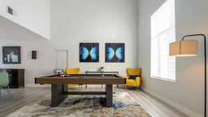 Una mesa de billar en una habitación de diseño moderno, con un ventanal grande, una lámpara y obras de arte en la pared.