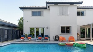 Una casa moderna de dos pisos con piscina, mobiliario exterior y patio cercado.
