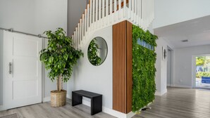 Un interior moderno con una escalera de madera, un espejo redondo, un banco y una pared cubierta de jardín vertical.