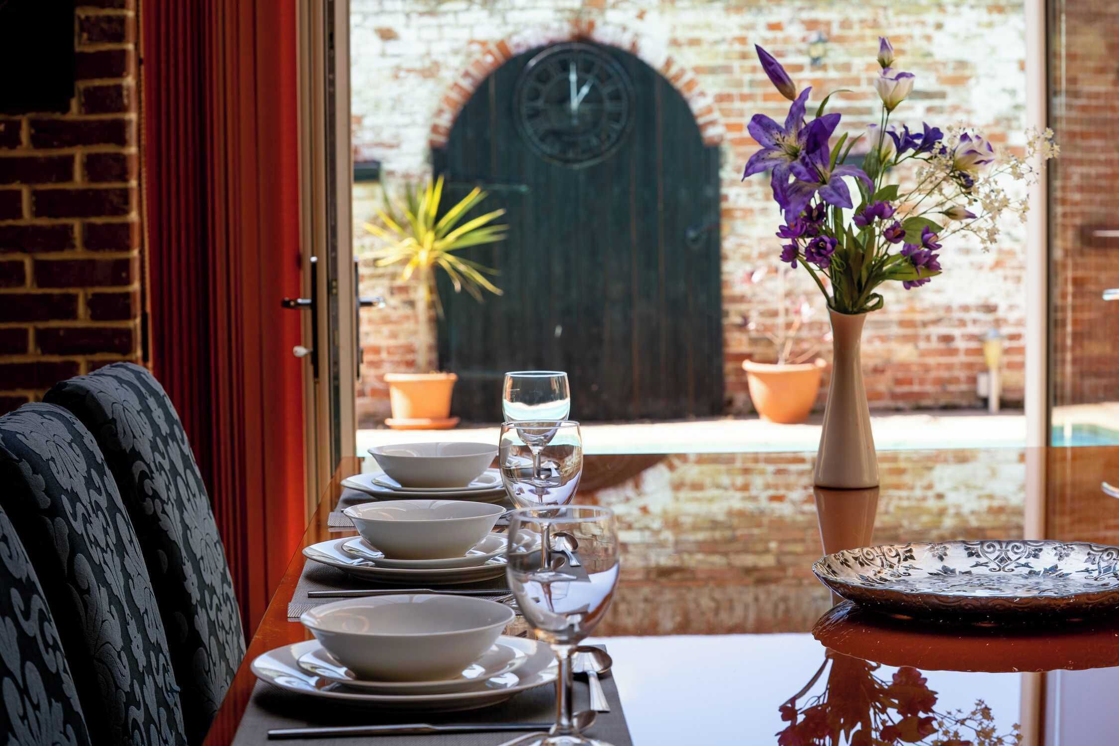 A dining table set with plates, bowls, and wine glasses, with a vase of flowers and a decorative plate on the table.