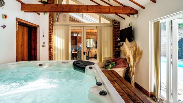 Ein Whirlpool in einem Raum mit Holzbalken, einer Backsteinwand und Blick ins Freie.