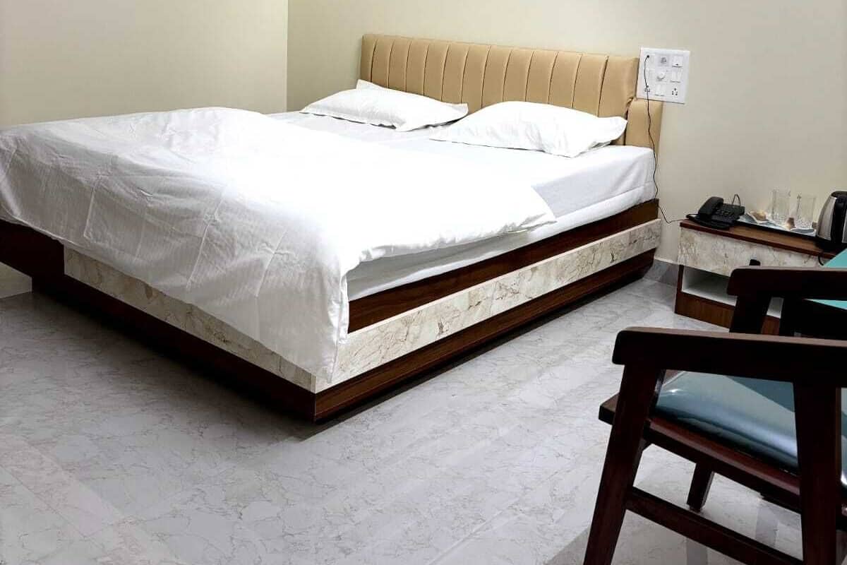 A bedroom with a bed, a bedside table, a chair, and a wall socket.