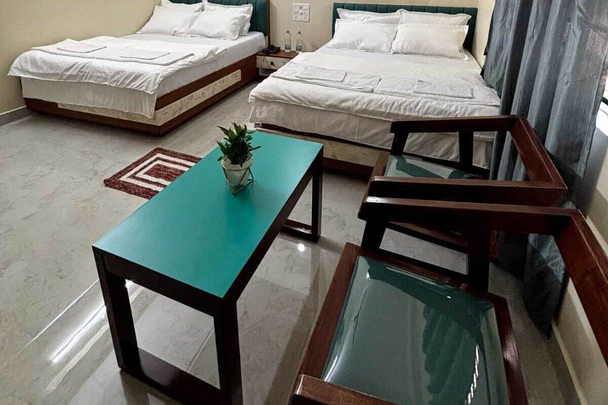 A hotel room with two single beds, a ceiling fan, a small table with a plant, and a glass-top table.