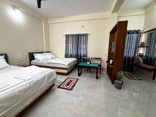 A hotel room with two beds, a desk, a chair, a TV, and a potted plant. - Evara Enclave Residency (Sullia)