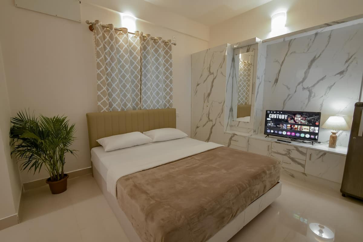 A hotel room with a bed, a TV, a plant, and marble walls.