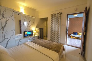 A hotel room with a bed, a TV, a desk with a lamp, and a bathroom visible through an open door. - HomeSlice Whitefield (Bengaluru)