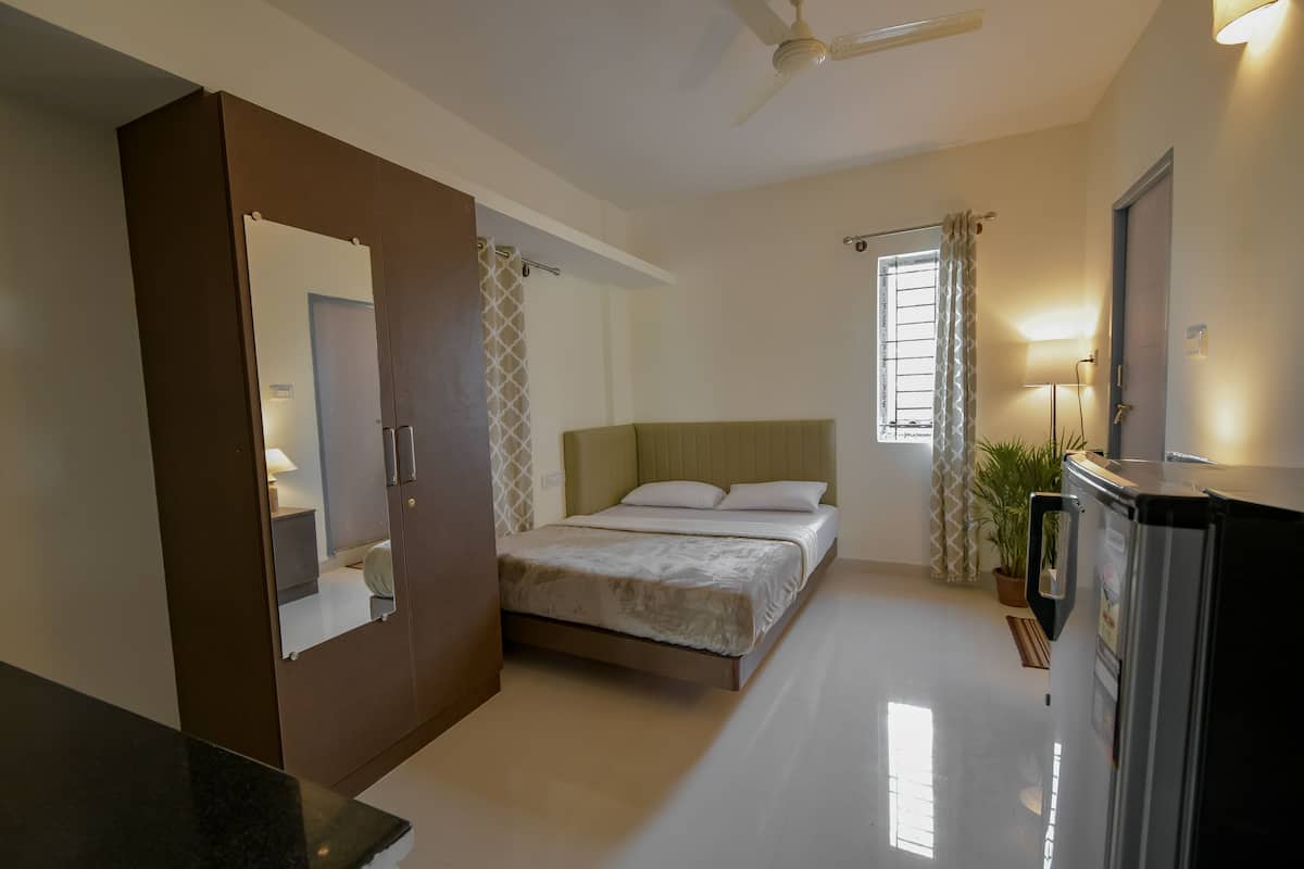 A bedroom with a bed, a wardrobe, a ceiling fan, a window with curtains, and a refrigerator.
