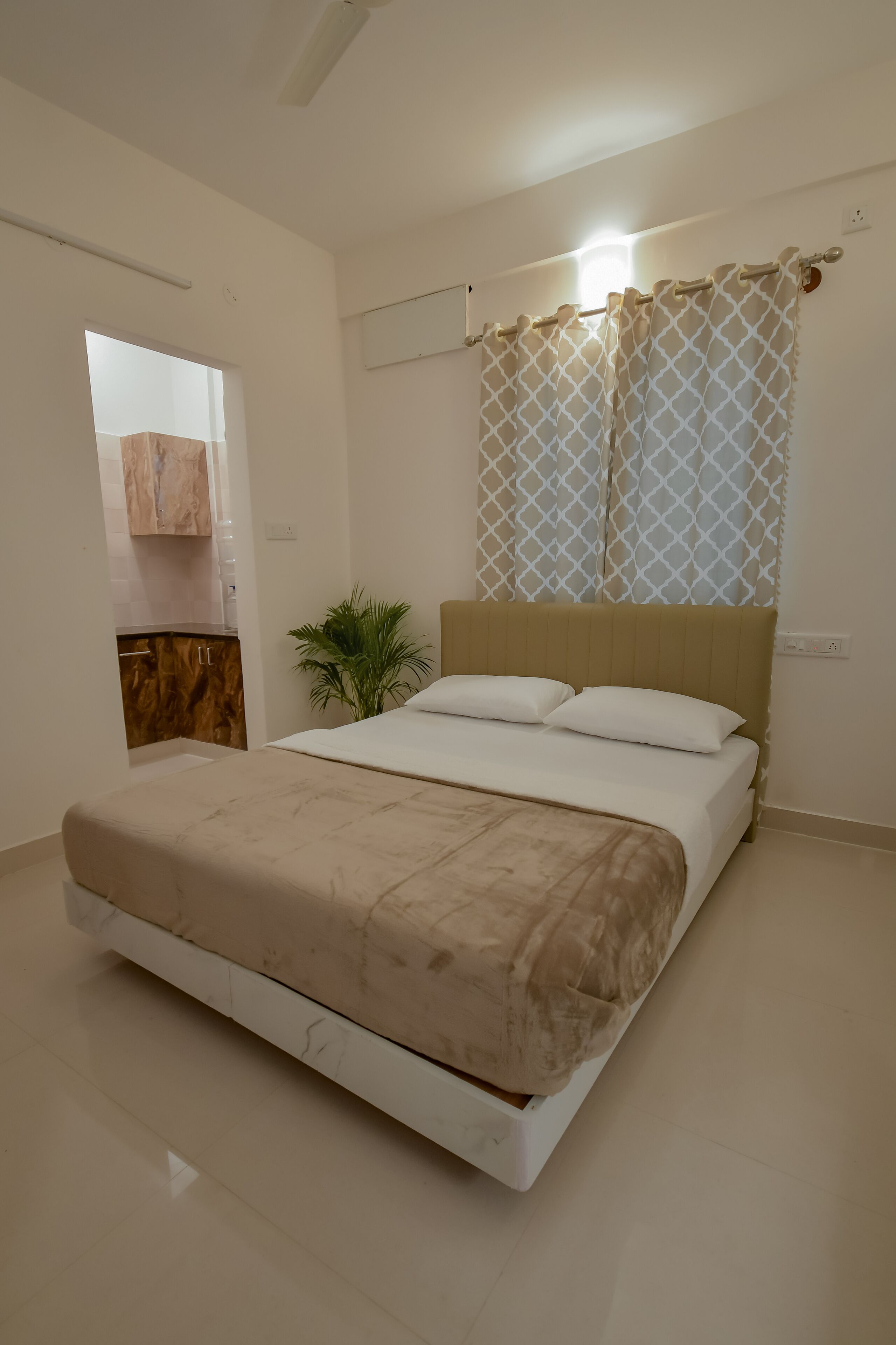 A bedroom with a bed, a nightstand, a potted plant, and a window with curtains.