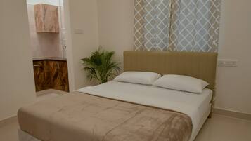 A bedroom with a bed, a nightstand, a potted plant, and a window with curtains.