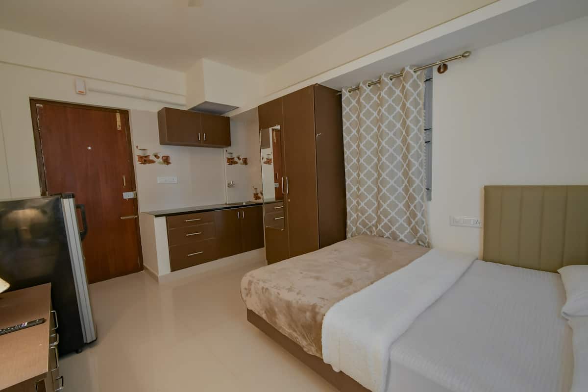 A bedroom with a bed, a nightstand, a wardrobe, and a kitchenette.
