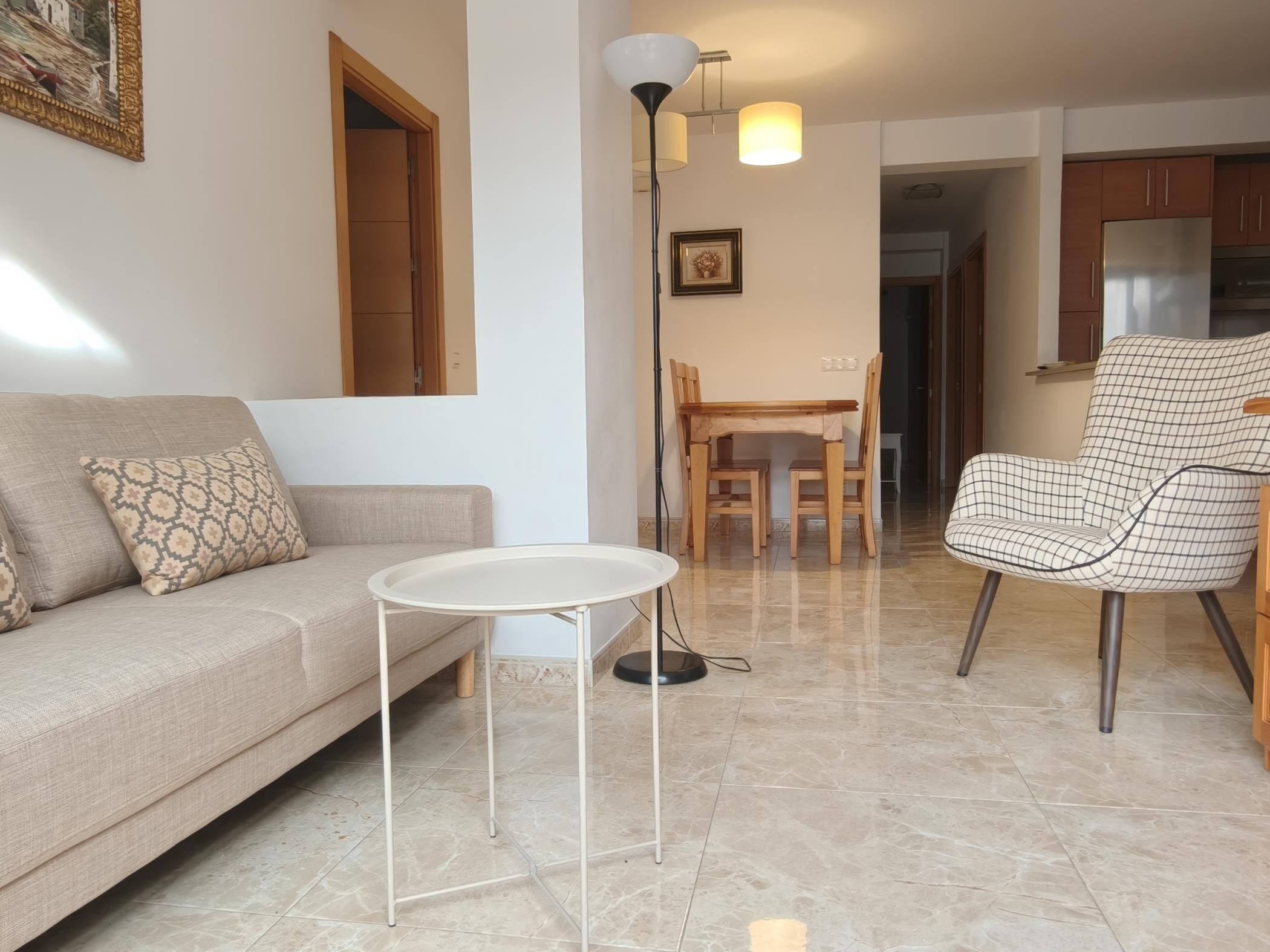A living room with a sofa, a small round table, a dining table with chairs, and a kitchen area with cabinets.