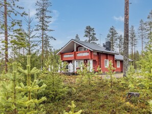 A red cabin with a porch, surrounded by dense forest.