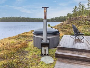 A sauna with a chimney, a wooden deck, and a bench overlooking a lake.