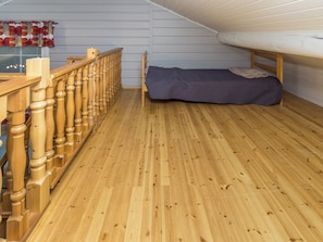 A room with a wooden floor, a bed with a blue cover, a wooden railing, and a window with blinds.