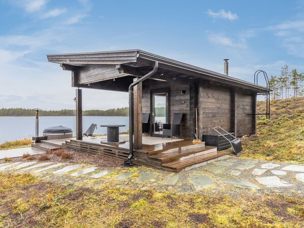 A modern cabin with a covered porch, outdoor seating, and a view of the lake.