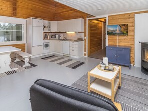 A modern kitchen with white cabinets, a microwave, and a stove. There is a dining table with a bench, a fireplace, and a television mounted on the wall.