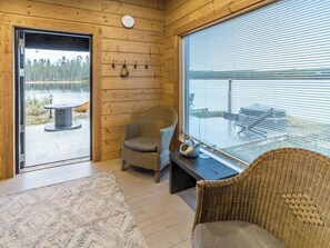 A wooden interior with a view of a lake, a wicker chair, a table, and a window with blinds. - Onnimanni by Interhome (Kuusamo)