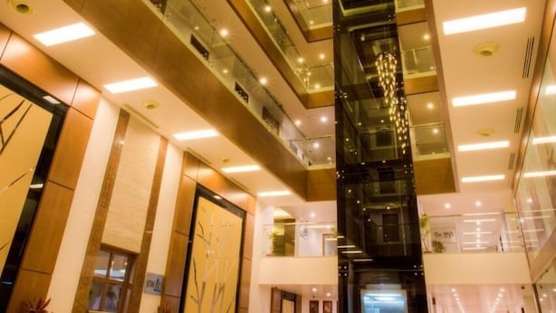 A modern lobby with a high ceiling, glass railings, and a central staircase. - The Atrium Boutique Hotel (Mysore)