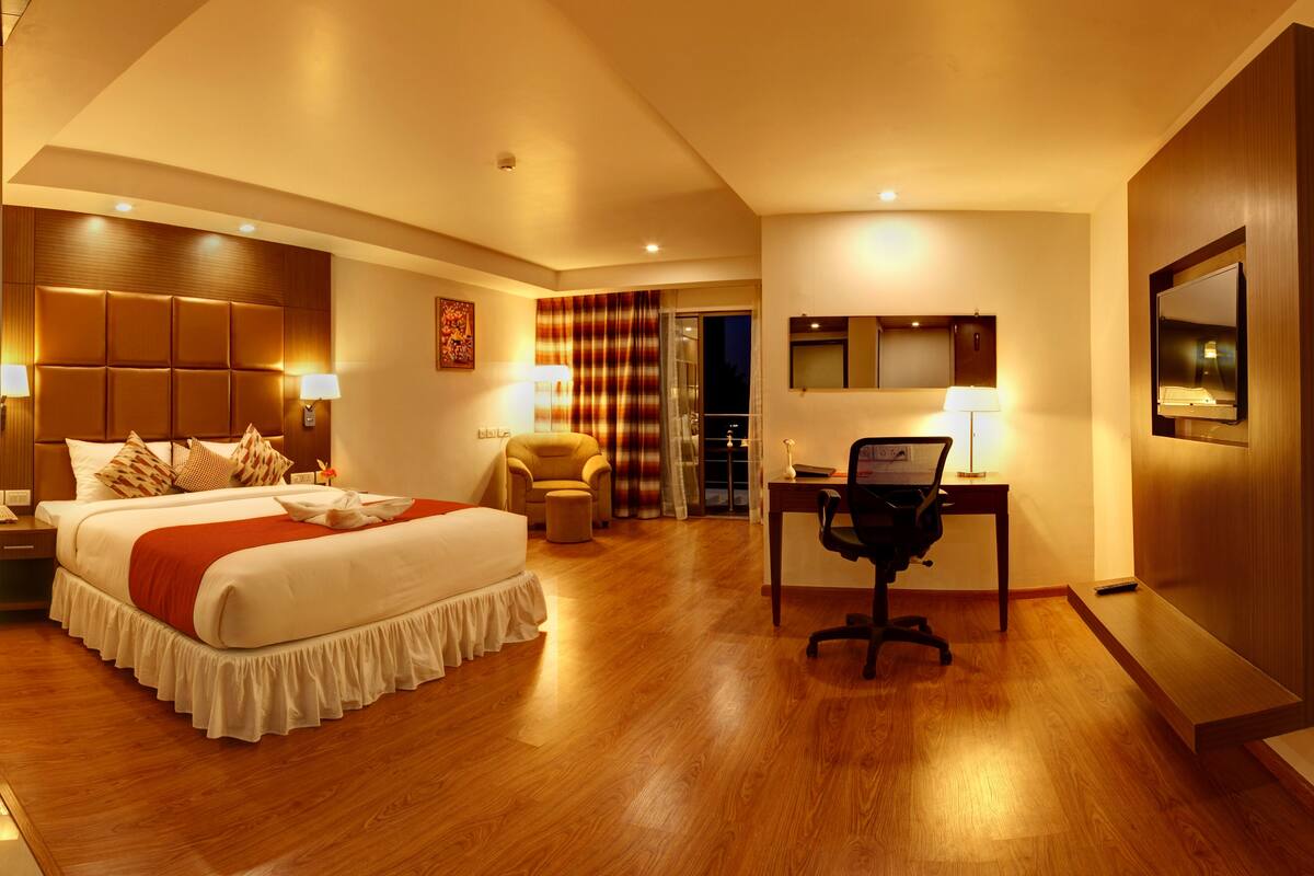A hotel room with a large bed, a desk with a chair, a television, and a bathroom with a shower and toilet.