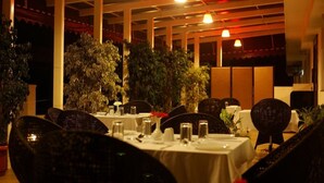 A restaurant with tables set for dining, surrounded by potted plants and a warm, dimly lit ambiance. - The Atrium Boutique Hotel (Mysore)