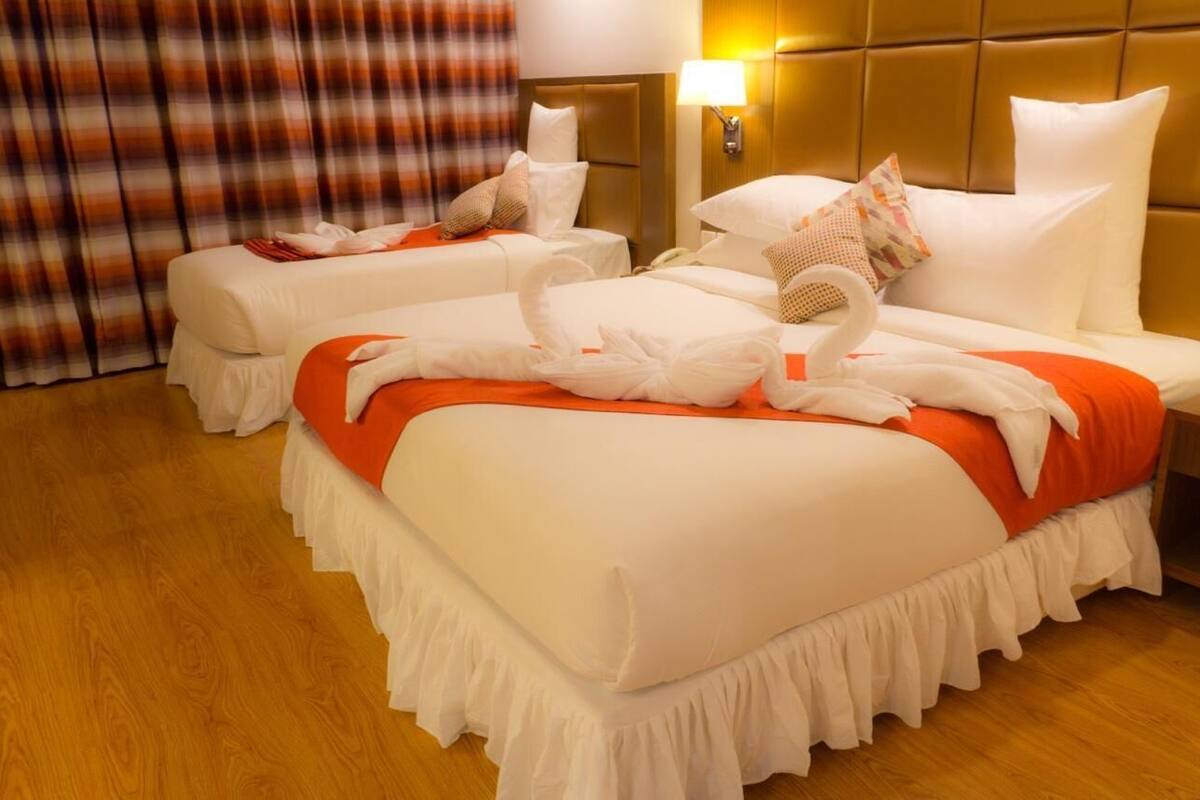 A hotel room with two beds, each with white bedding and orange accents, and a wooden floor.