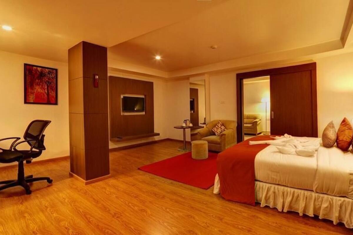 A hotel room with a bed, bedside table, lamp, chair, and a red carpet.