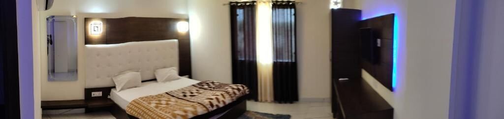 A bedroom with a bed, a nightstand, a TV, and a wall-mounted light fixture.