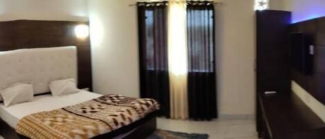 A bedroom with a bed, a nightstand, a TV, and a wall-mounted light fixture.
