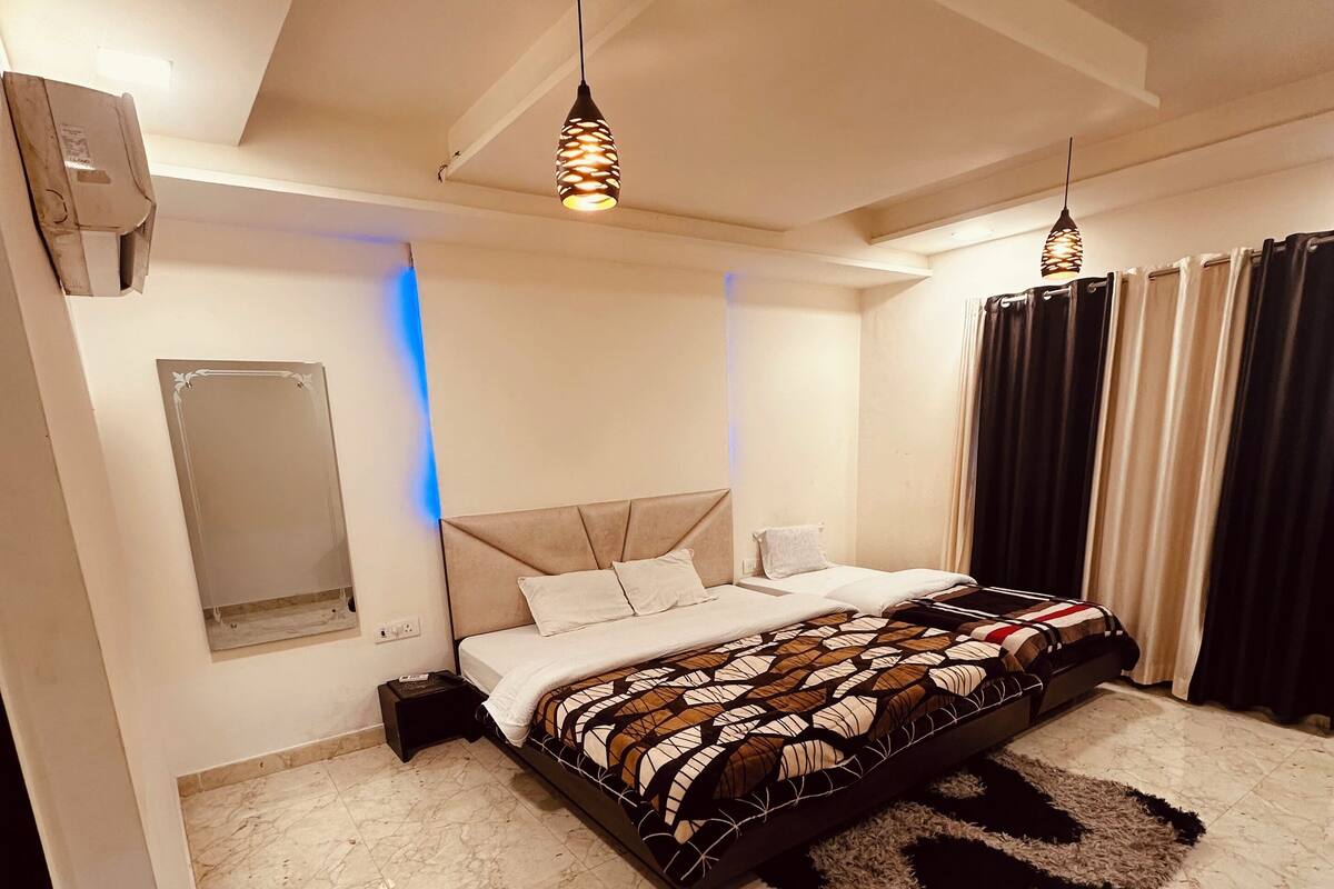Une chambre à coucher avec un lit, deux lampes suspendues, un miroir, une fenêtre avec des rideaux et un sol en marbre.