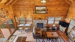Interior acolhedor de uma cabana de madeira com lareira, móveis de madeira e um ventilador de teto.