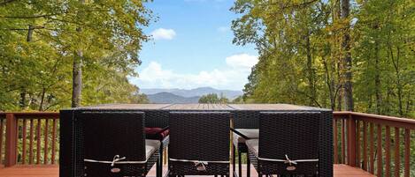 Une terrasse avec une table et des chaises, donnant sur une zone boisée et offrant une vue sur des montagnes au loin.