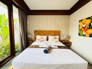 A hotel room with a large bed, two bedside tables with lamps, a wooden headboard, and a large window with curtains. - Lavilla Ubud (Sukawati)