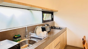 A modern kitchen with a stainless steel sink, a dish rack, a stove, and a window above the sink.