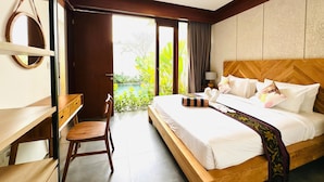 A hotel room with a bed, a desk, and a chair. There is a view of greenery outside the window.