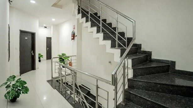 A modern hotel lobby with a staircase, a reception desk, and potted plants. - Hotel Vishnu Residency Inn (Amritsar)