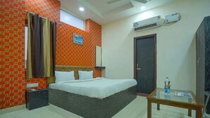 A hotel room with a bed, a small table, an air conditioning unit, and a window with curtains. - Hotel Vishnu Residency Inn (Amritsar)
