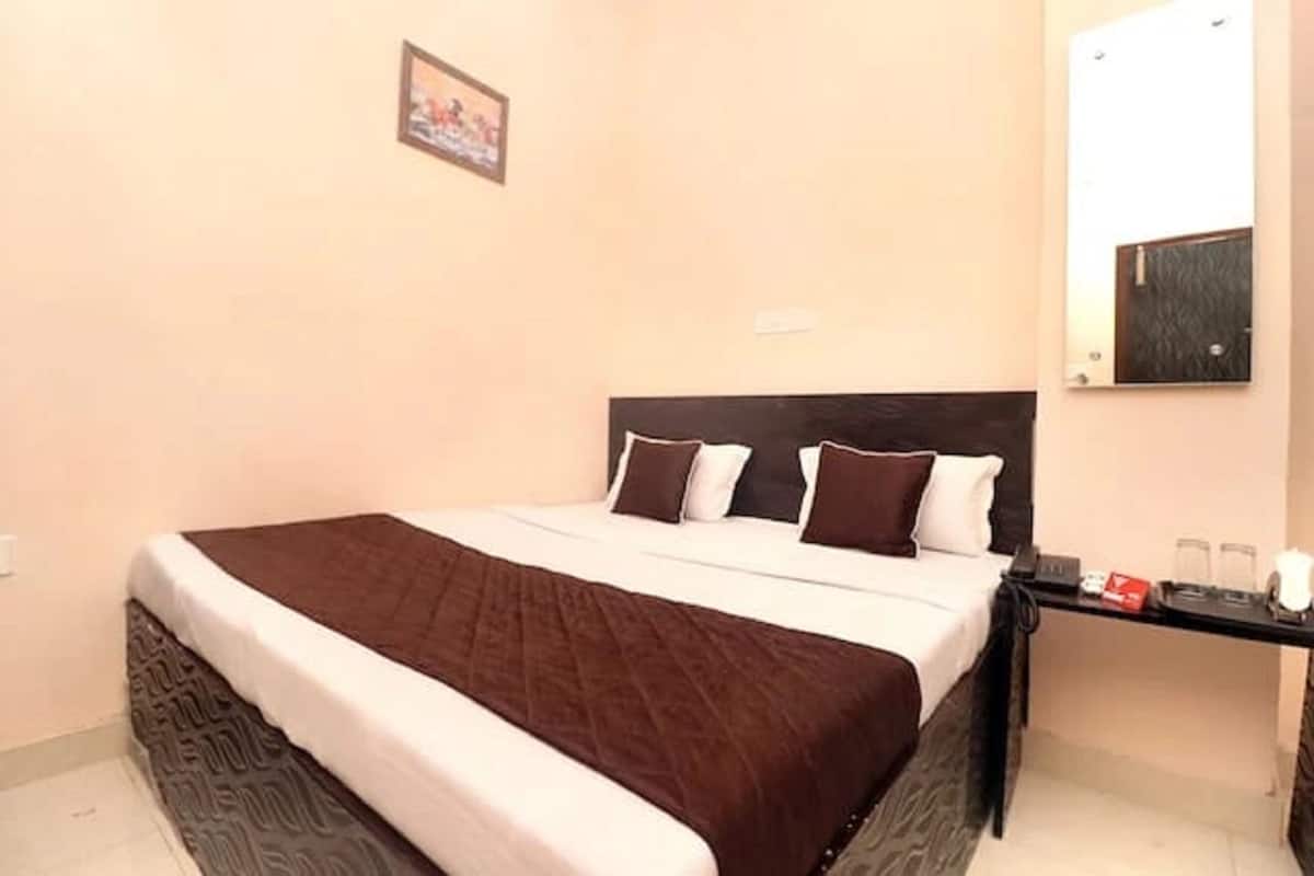 Quarto de hotel com cama, mesa de cabeceira com telefone e óculos, e espelho fixado na parede.