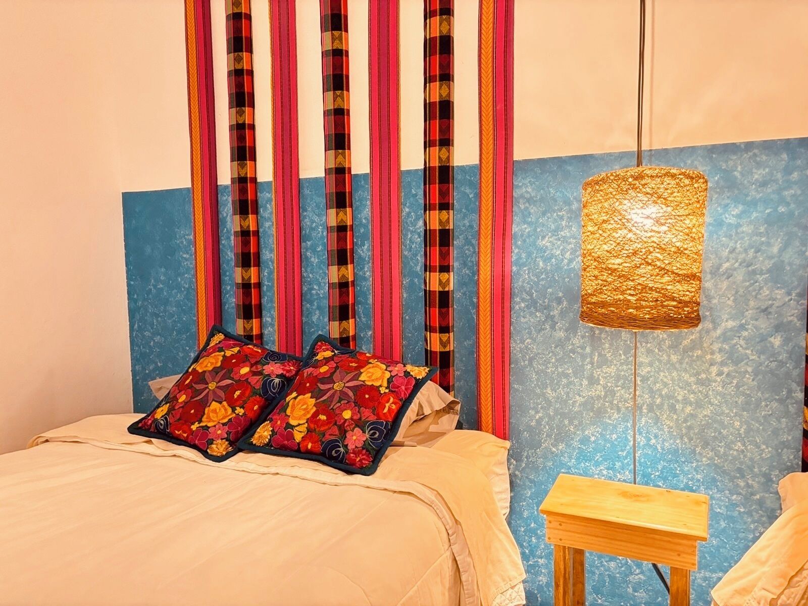 Un lit avec des coussins à motifs floraux, une lampe suspendue et une table de chevet en bois.