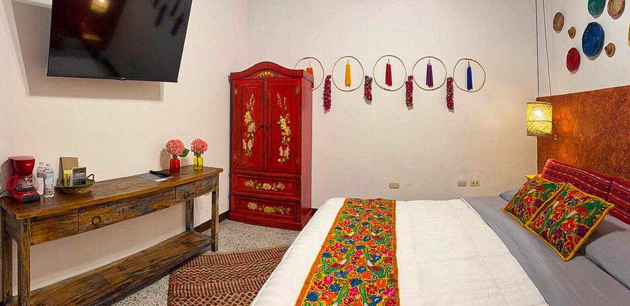 A bedroom with a bed, a wooden desk, a red cabinet, a television, and wall decorations.