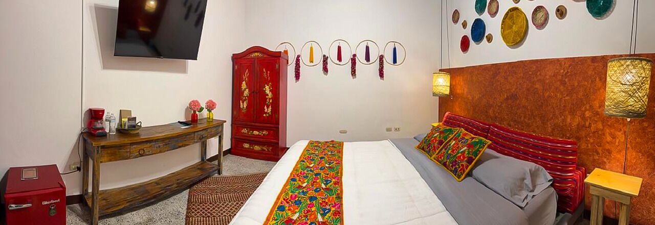 A bedroom with a bed, a wooden desk, a red wardrobe, a TV, and wall decorations.